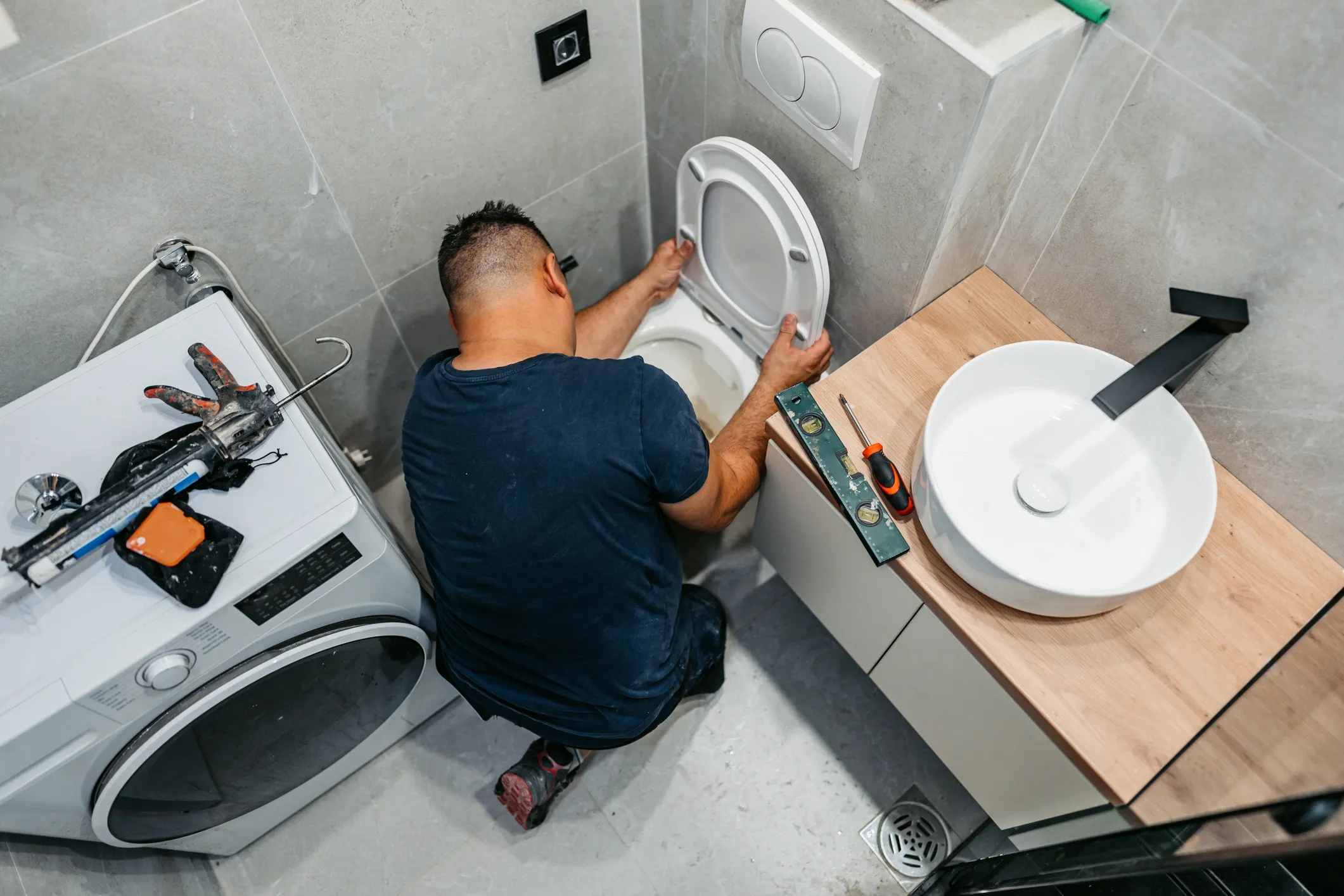 Person fixing a toilet in bathroom.